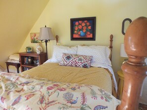 A bedroom with a bed, a nightstand, a lamp, a painting, and a wooden chair. - Montrose Farms Alpaca Ranch (Brownsburg)