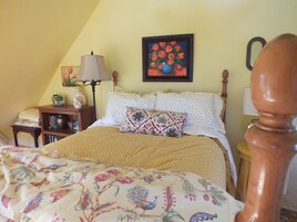 Un dormitorio con cama, mesita de noche, lámpara, un cuadro y una silla de madera.