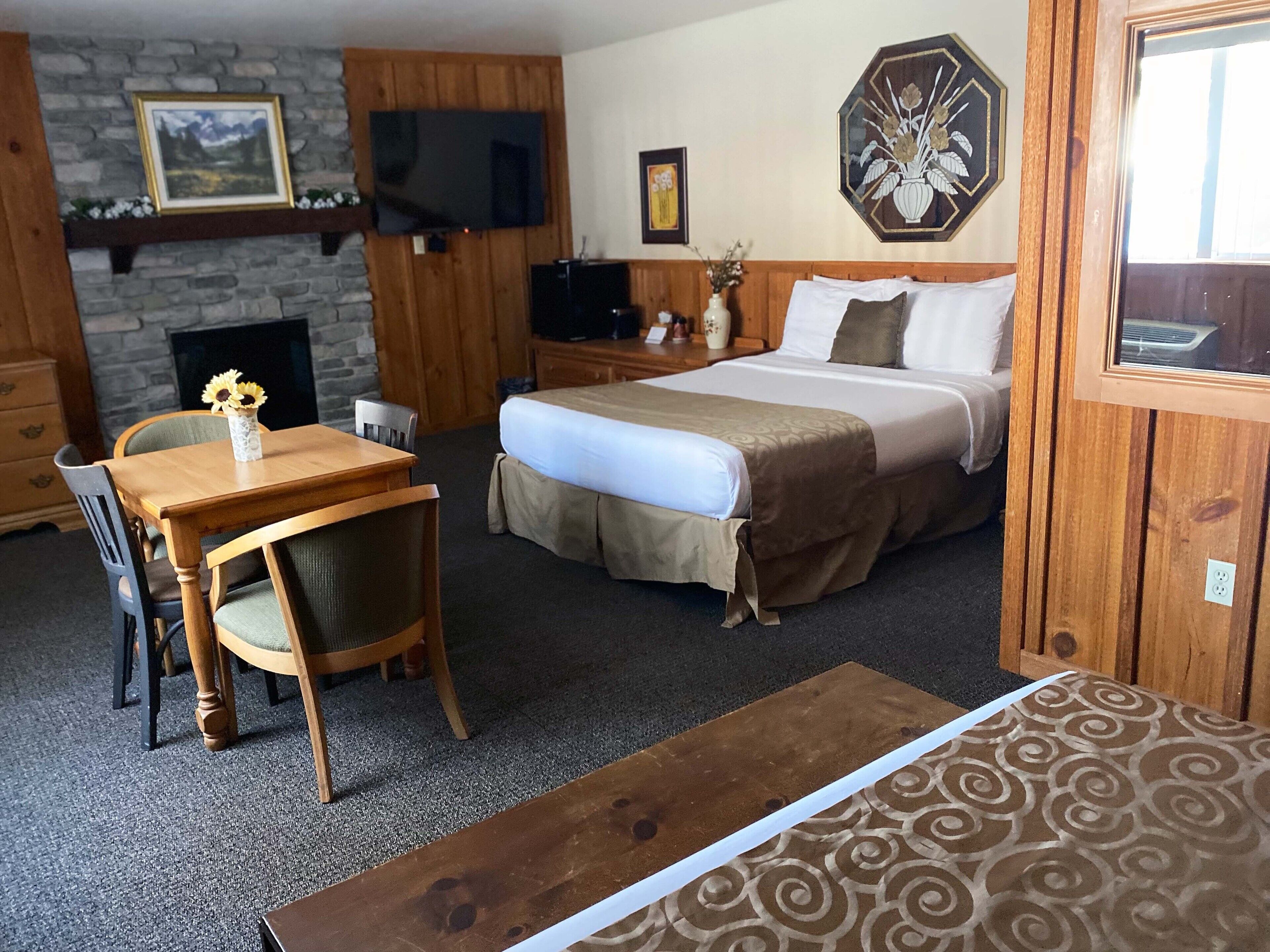 Habitación de hotel con cama, televisor, chimenea y zona de comedor con mesa y sillas.