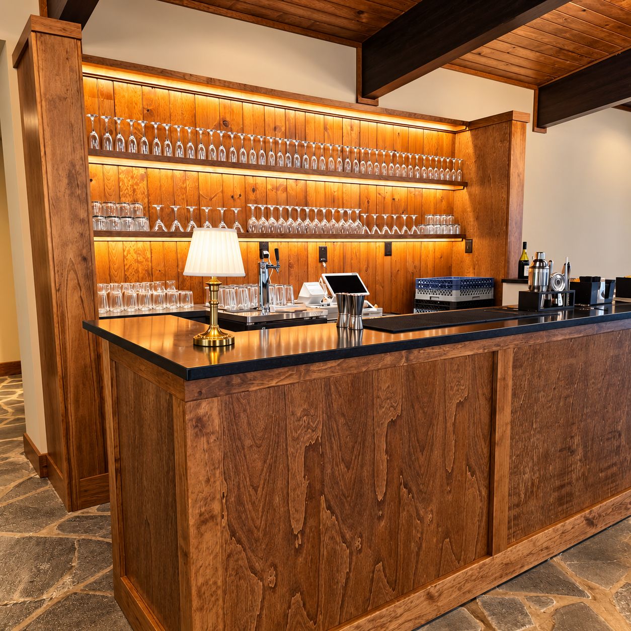 A bar area with a wooden counter, a cash register, and a wine glass rack.