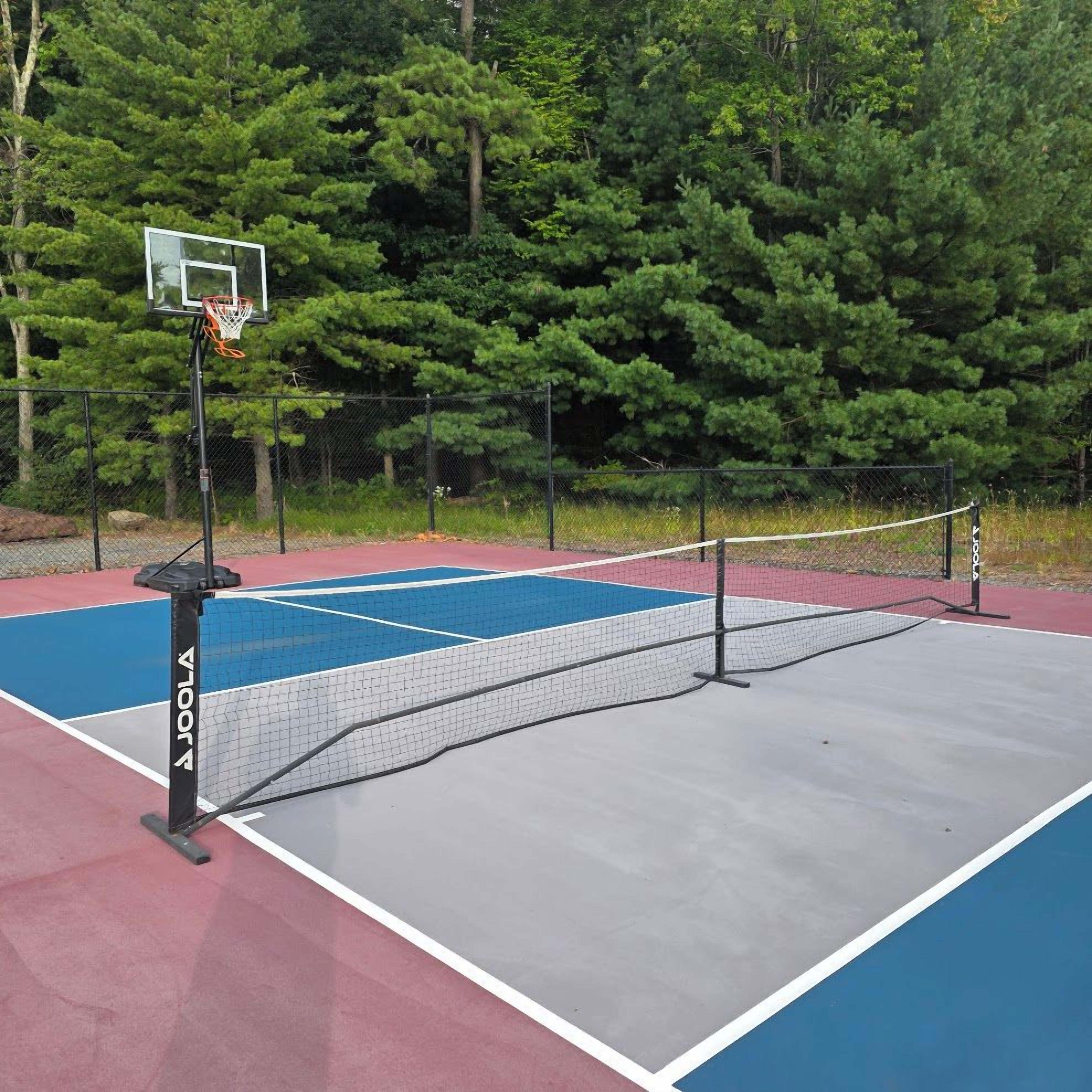 An outdoor tennis court with a net, surrounded by a fence and trees.