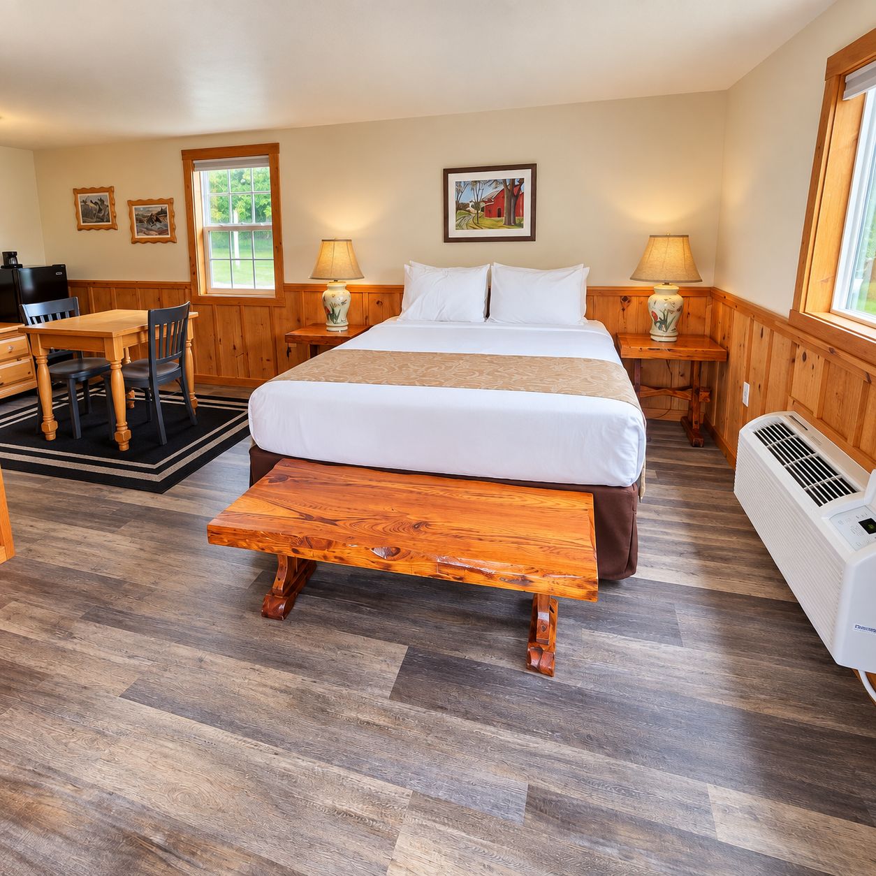 A hotel room with a large bed, a wooden bench, a desk, and a chair. There are two bedside tables with lamps.