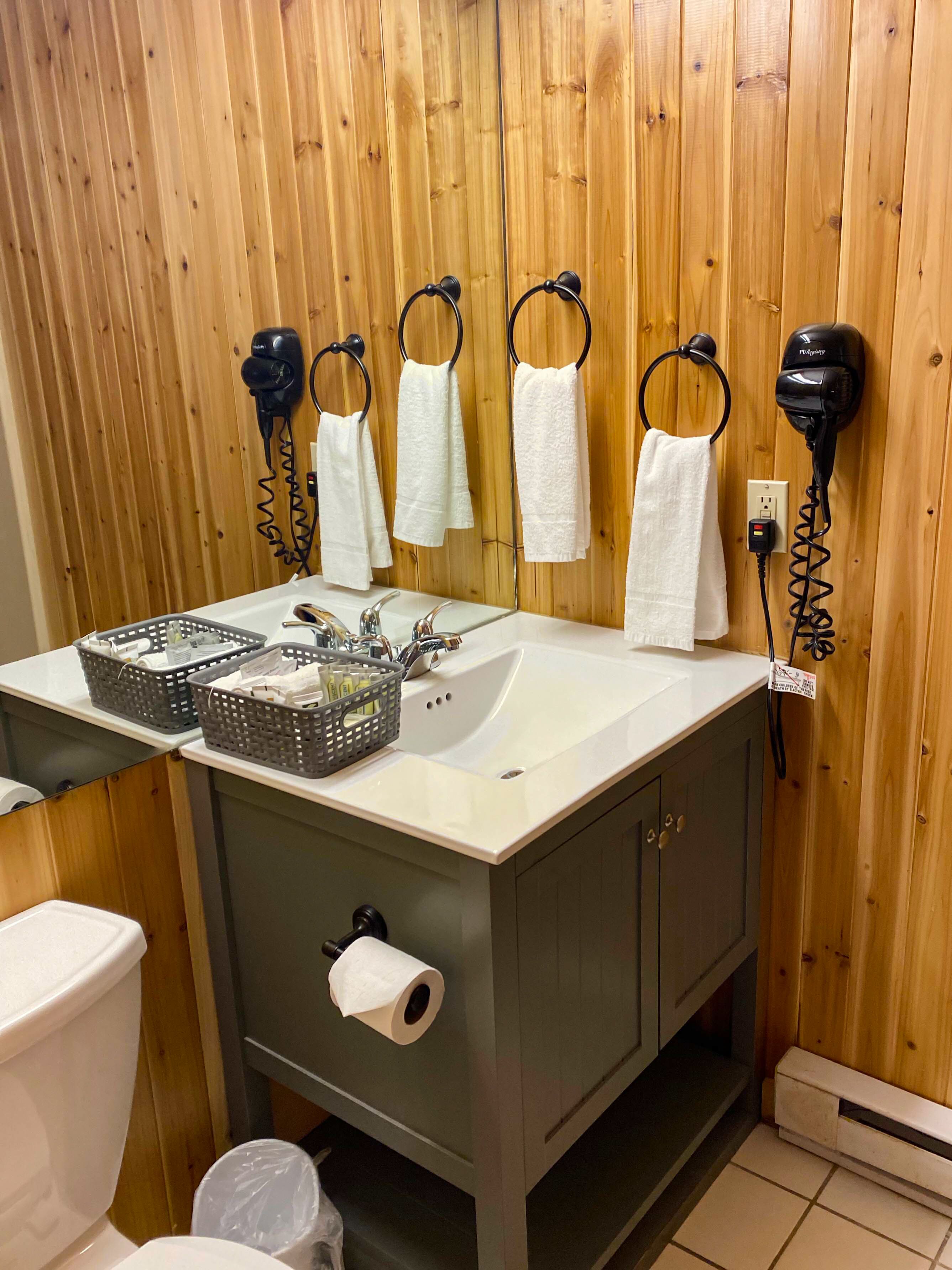 A bathroom with wooden paneling, a sink with a mirror, and two hair dryers mounted on the wall.