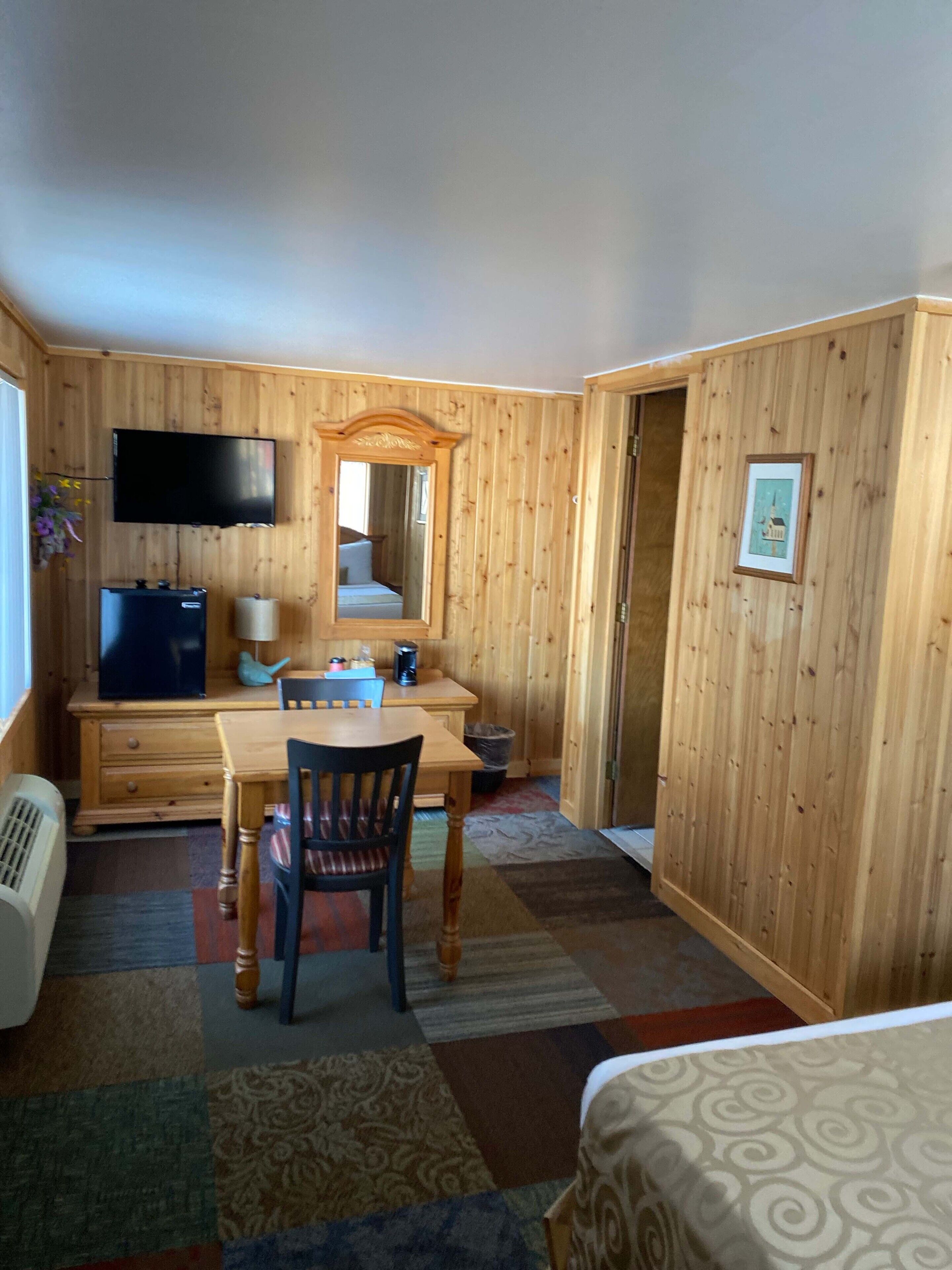 Een kamer met houten lambrisering, een flatscreen televisie, een bureau met stoel, een bed en een lijst met een afbeelding aan de muur.
