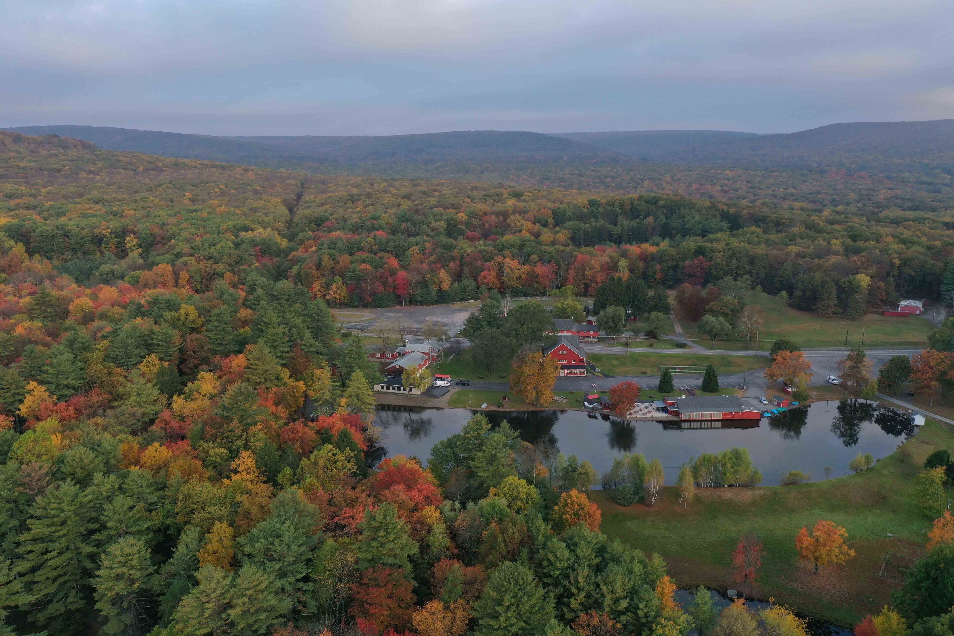 A rural landscape with a lake, a red barn, and surrounding trees in autumn colors.