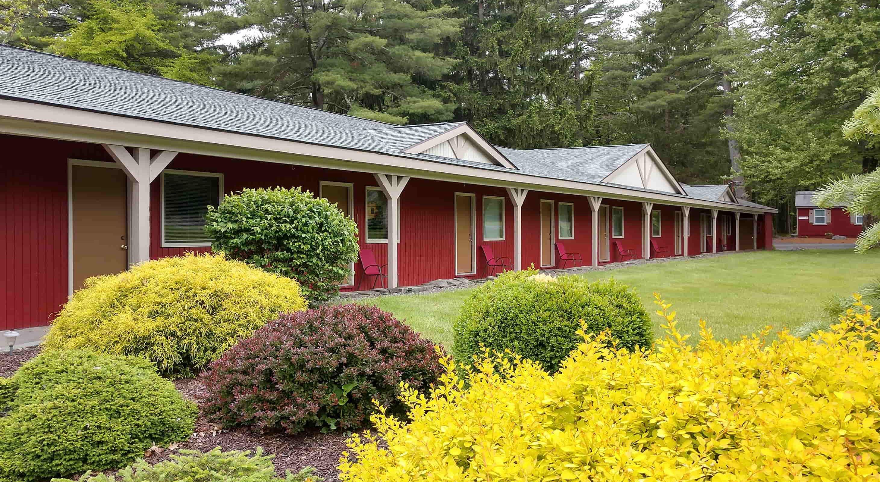 A row of red buildings with individual doors, surrounded by well-maintained lawns and various shrubs.