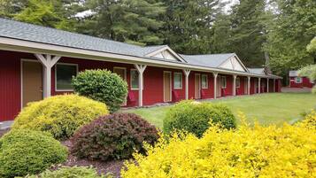 A row of red buildings with individual doors, surrounded by well-maintained lawns and various shrubs.