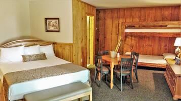 A room with a bed, a bench, a table with chairs, and a bunk bed.