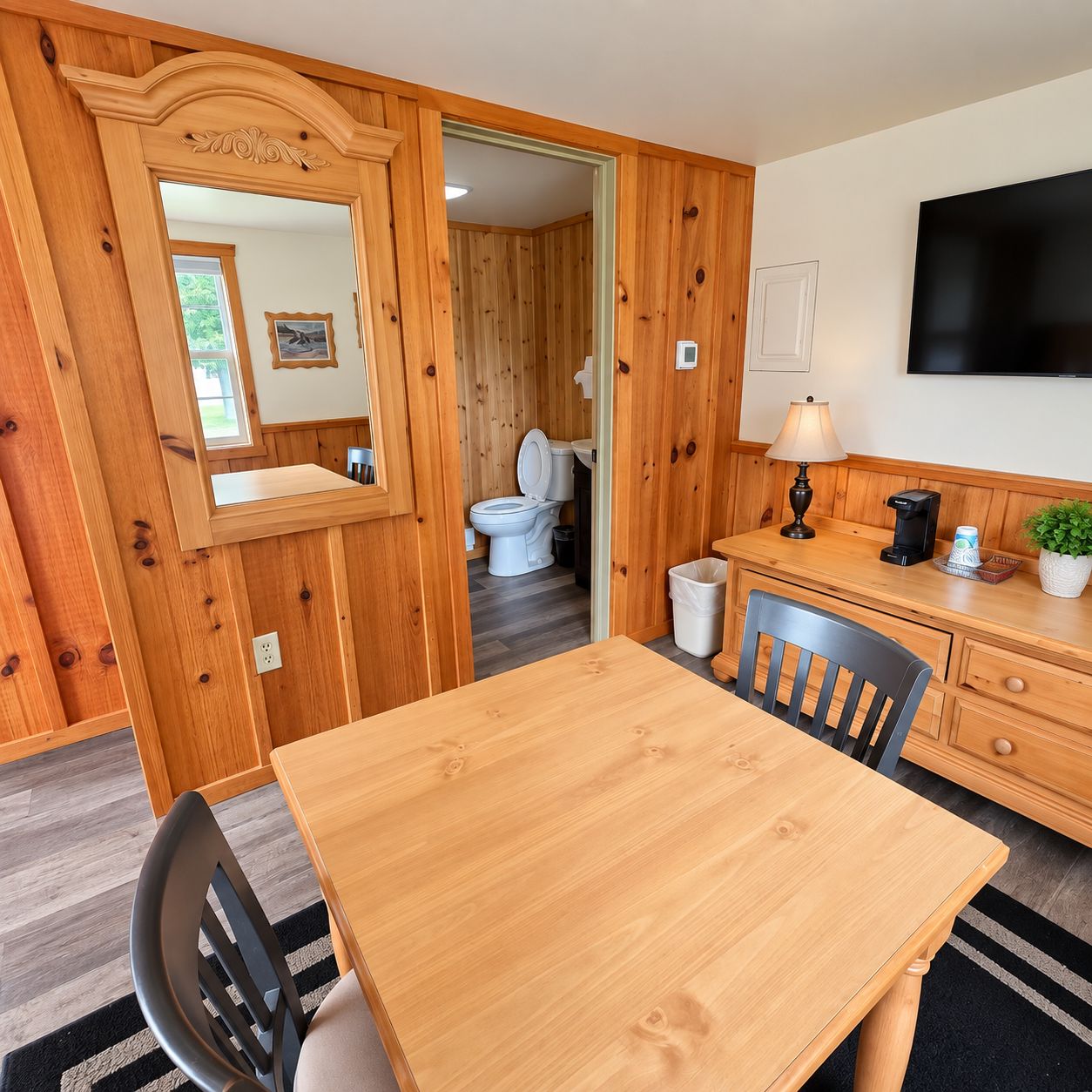 A wooden-paneled room with a dining table, chairs, a TV, and a small kitchenette.