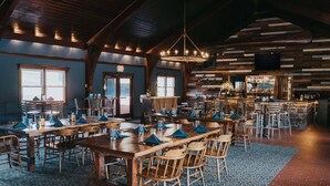 Un comedor amplio con largas mesas y sillas de madera, una zona de bar con mostrador de piedra y un candelabro colgando del techo.