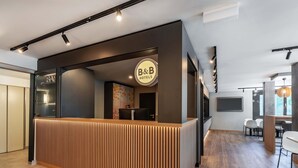 Taulell de recepció amb un cartell de 'B&B', un disseny de panell de fusta i un interior modern amb televisió de pantalla plana i zona de seients.
