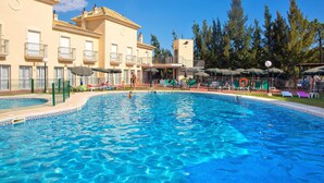A swimming pool with a clear blue water, surrounded by lounge chairs and umbrellas, and a building with balconies in the background. - Interpass Golf Playa Country Club (Isla Cristina)