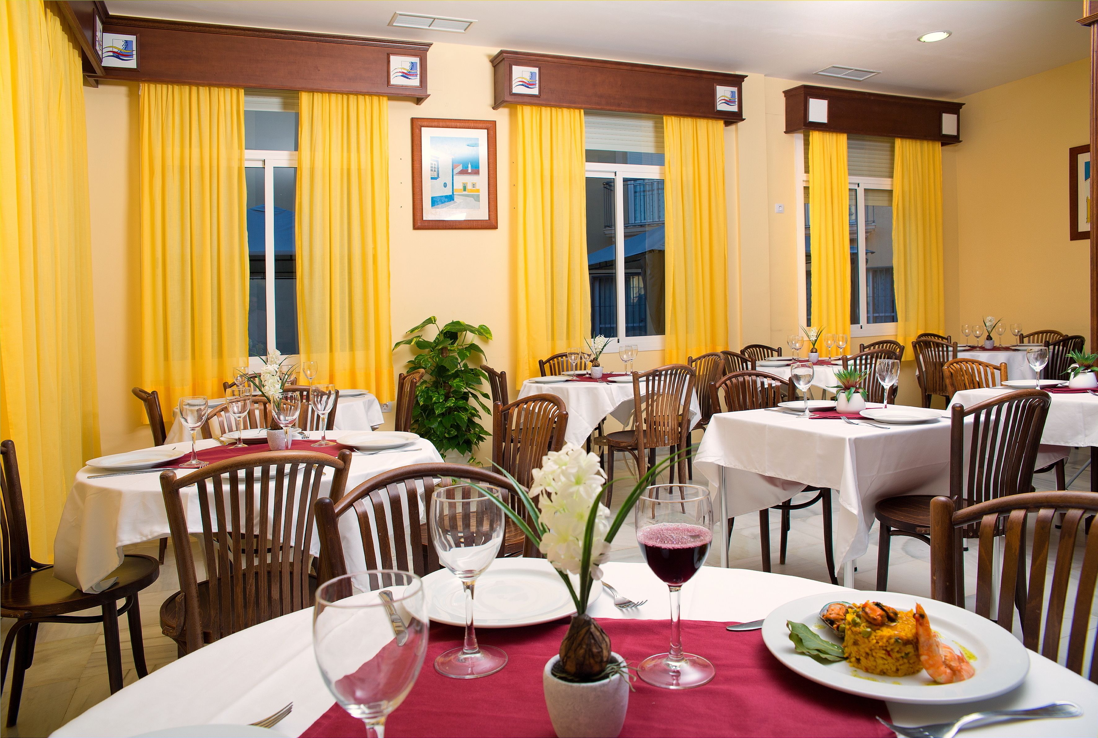 Un comedor con varias mesas, sillas y cortinas amarillas.