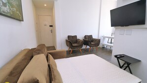 Ein Hotelzimmer mit einem großen Bett, zwei Sesseln, einem kleinen Tisch und einem flachbildfernseher an der Wand.