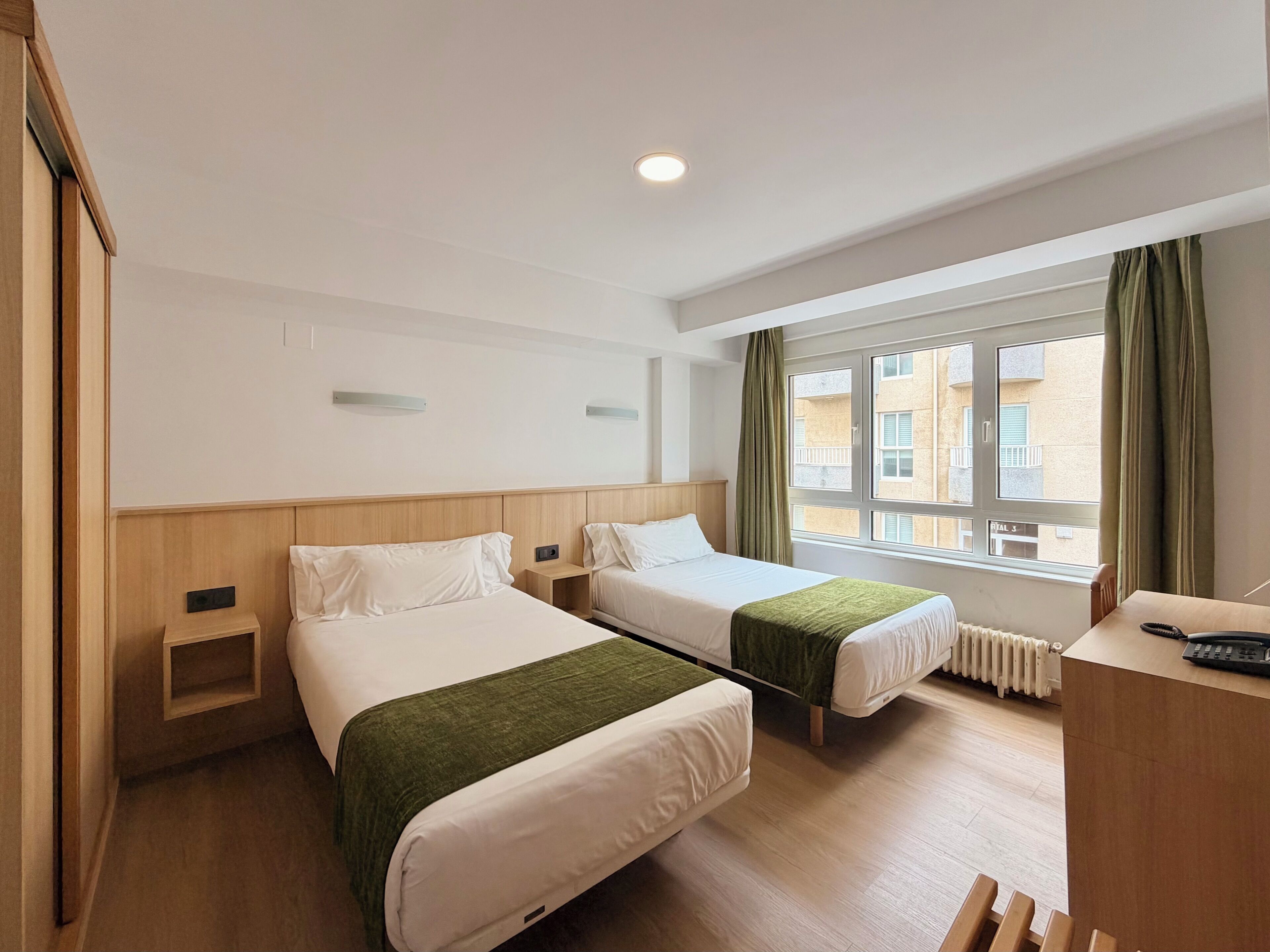 Habitación de hotel con dos camas, un escritorio, una ventana con cortinas y un radiador.