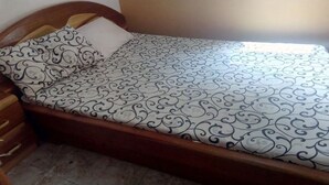 Un lit simple avec une couvre-lit à motifs et des oreillers, une tête de lit en bois et une fenêtre avec des rideaux.