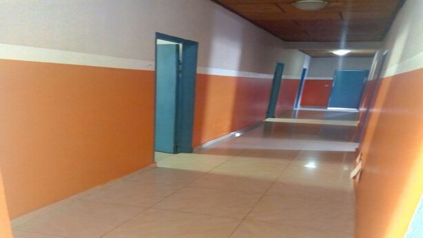Un couloir aux murs orange et blancs, doté d’un sol carrelé et de portes donnant sur différentes pièces.