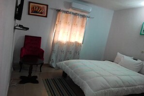 A bedroom with a bed, a red chair, a curtain, and an air conditioning unit. - Villa Onelis (Abidjan)