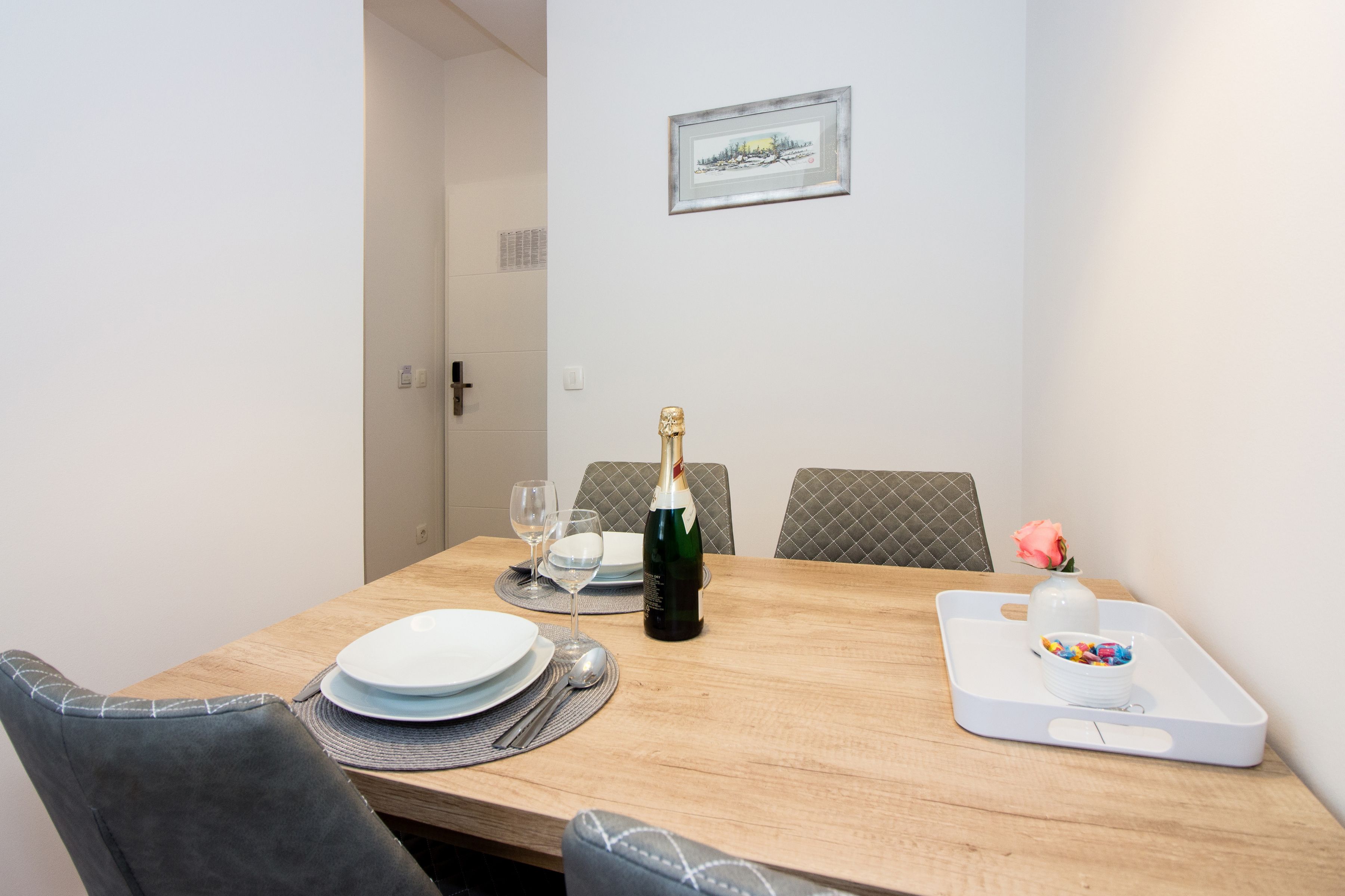 A dining table set with plates, glasses, a bottle of champagne, and a tray with a vase and candy.