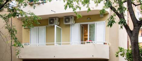 Un immeuble doté d’un balcon, de climatiseurs et d’un arbre.