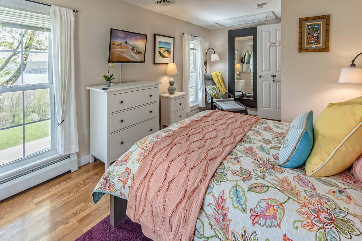 A bedroom with a bed, dresser, nightstand, and a window with curtains.