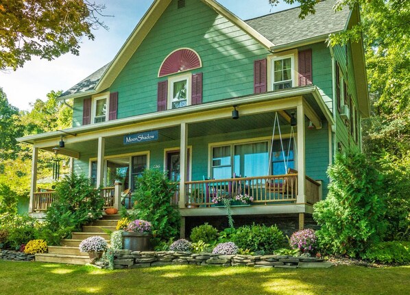 A two-story house with a porch, labeled "Moore Shadow," surrounded by a well-maintained garden with various plants and flowers. - Moonshadow Bed and Breakfast (Hammondsport)