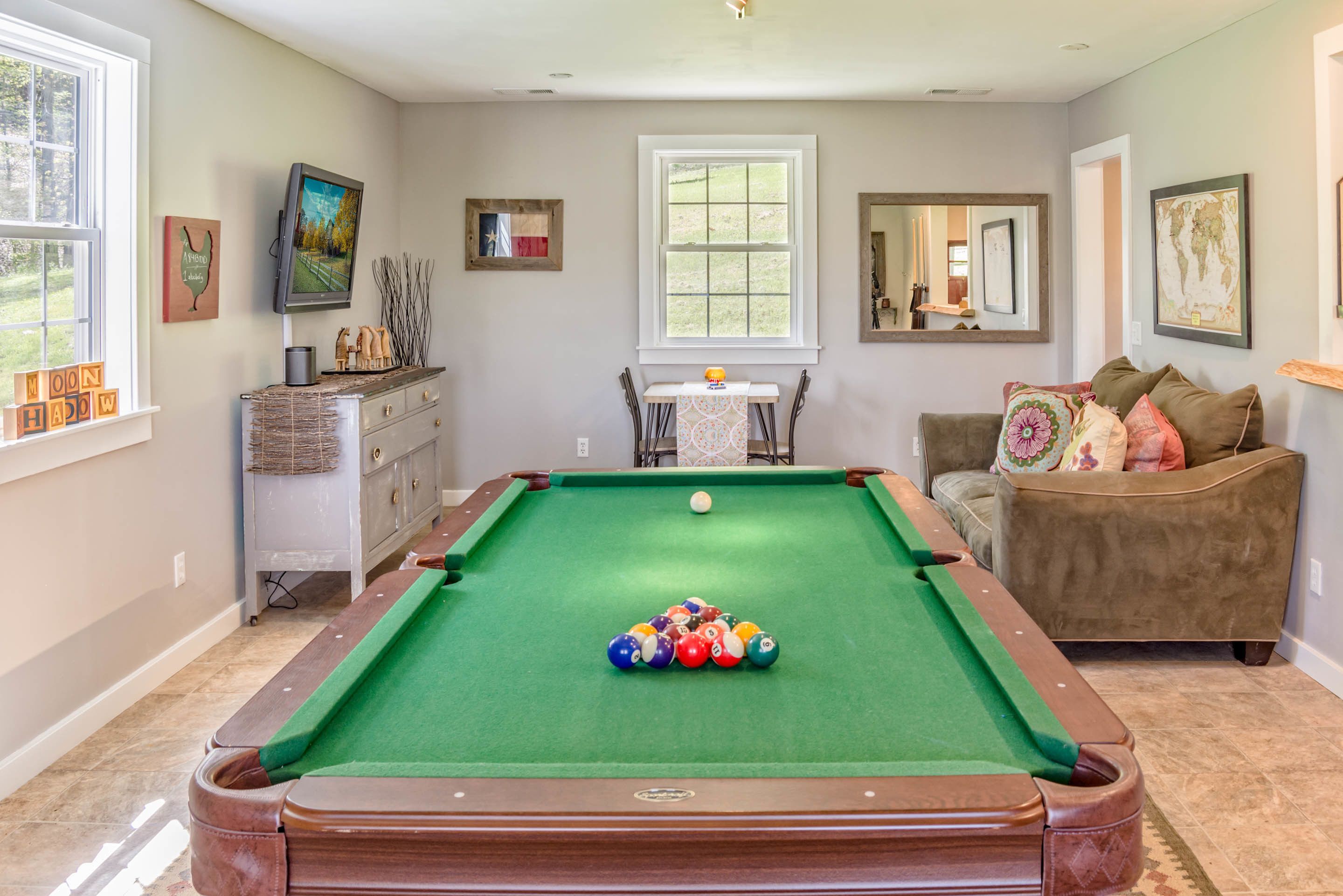 A pool table with balls, a sofa, a television, and artwork on the walls.