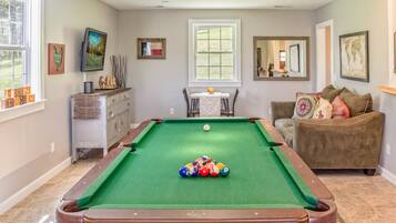 A pool table with balls, a sofa, a television, and artwork on the walls.