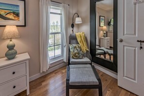 A modern room with a bench, a lamp, a window with curtains, a small table, and a mirror. - Moonshadow Bed and Breakfast (Hammondsport)