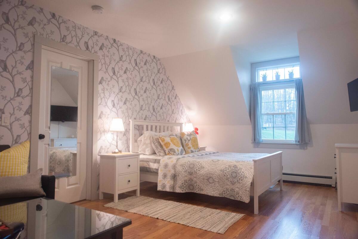 A bedroom with a bed, bedside tables, a mirror, a window with curtains, and a radiator.