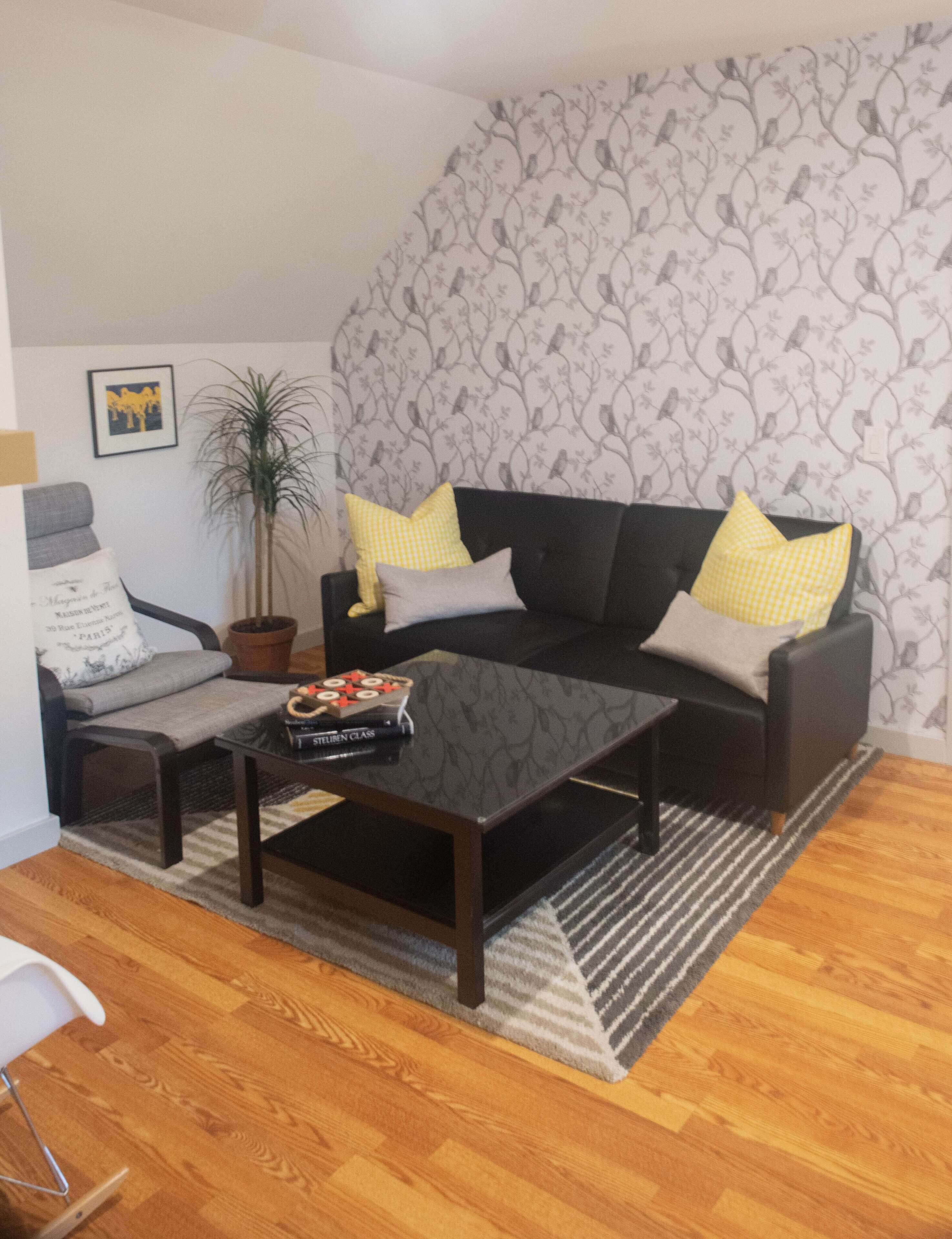 A living room with a dark sofa, two armchairs, a coffee table, and a potted plant.