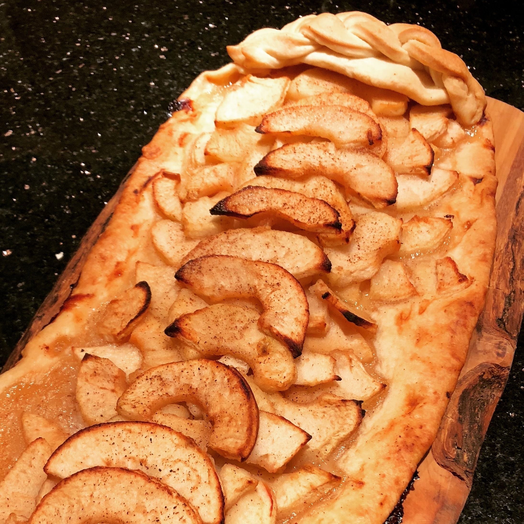 A rectangular wooden board with a baked dish on top, featuring apple slices and a dollop of cream.