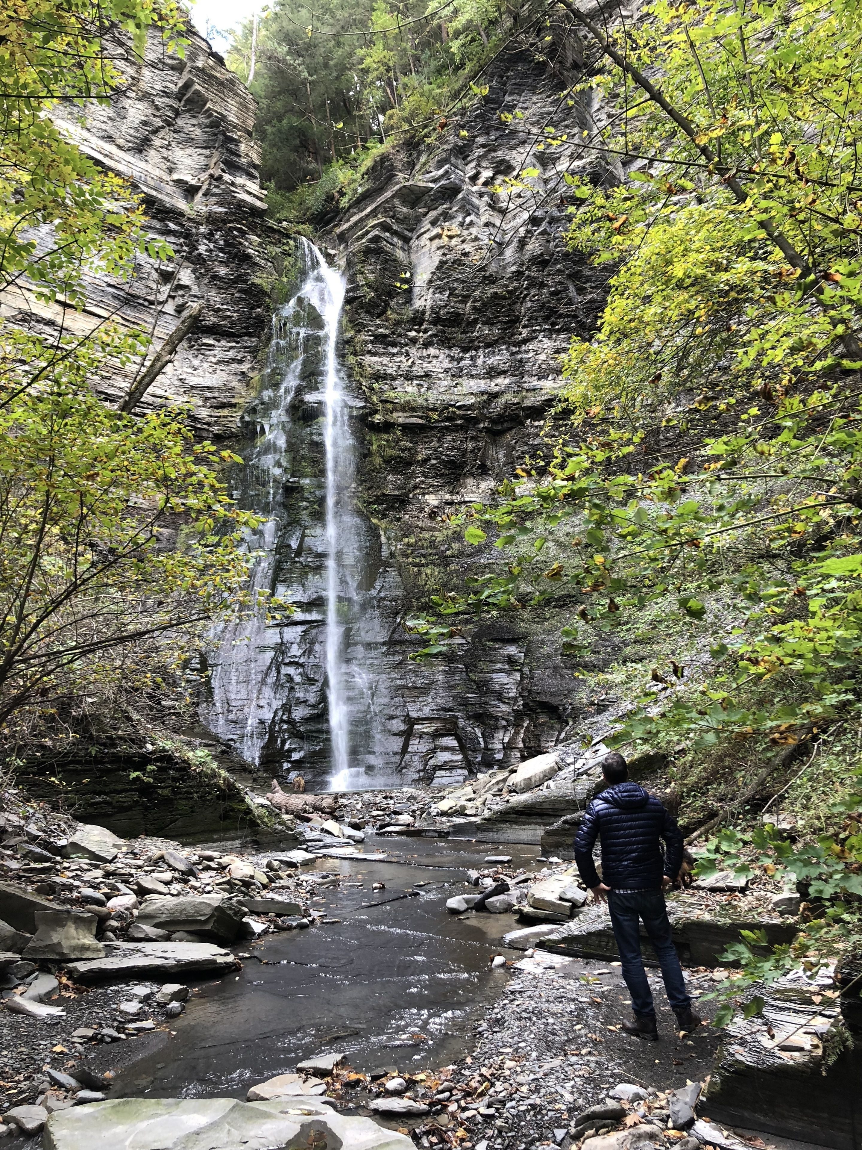 A waterfall in a rocky gorge with a person standing at the base.