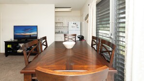 A dining table with chairs, a television, and a kitchen in the background.