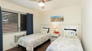 Ein Schlafzimmer mit zwei Betten, einem Deckenventilator, einem Fenster mit Jalousien, einem Heizkörper und einem Bild an der Wand.