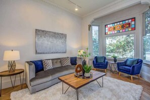 Una sala de estar con sofá, sillas, una mesa de centro, lámpara, planta y un vitral.