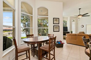 A spacious living area with a round wooden table, comfortable seating, a sofa, and a ceiling fan.
