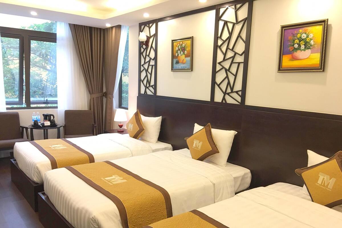 A hotel room with three beds, a desk, a chair, and a window with curtains.