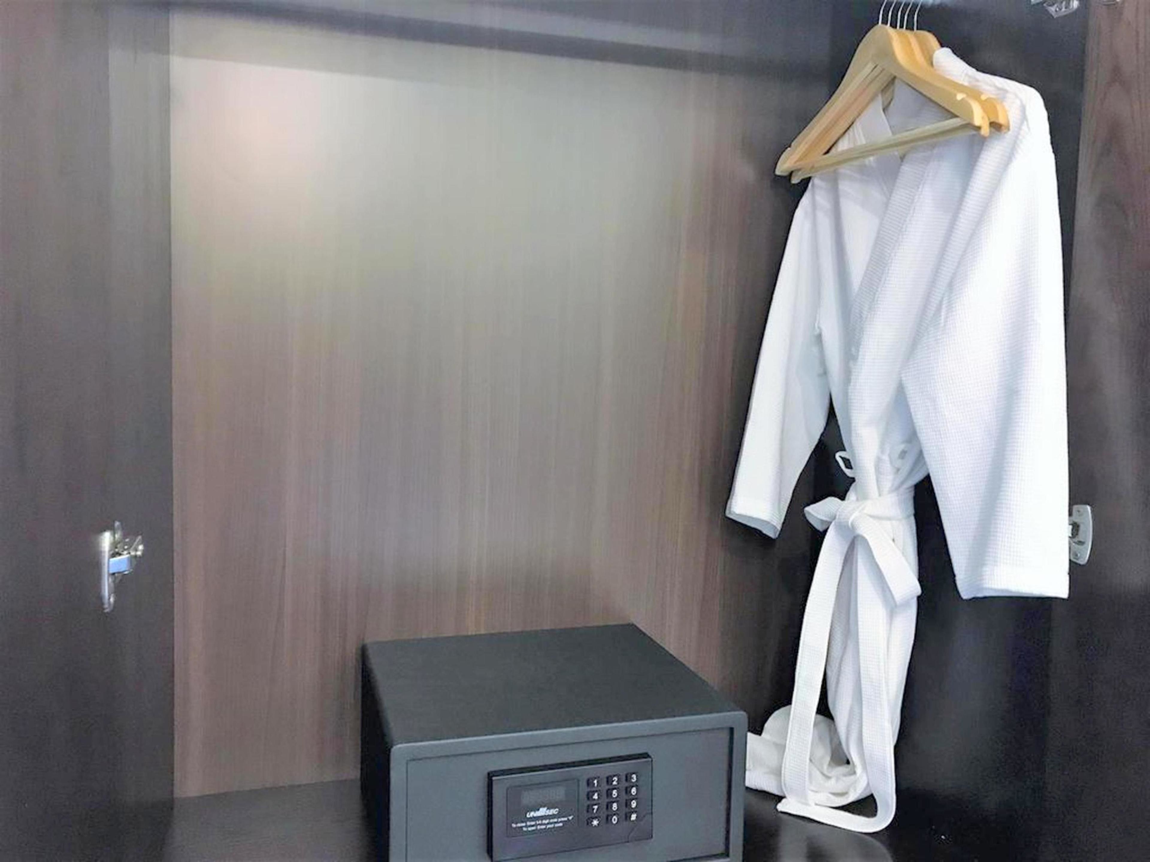 Una camera d'hotel con un minibar, un accappatoio appeso a un appendiabiti in legno e una porta con maniglia.