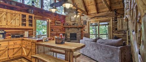 A rustic cabin interior with a wooden dining table, bench, sofa, and a fireplace.