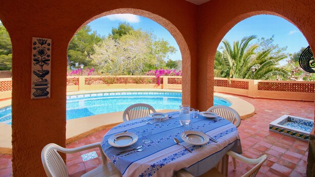 An outdoor dining area with a pool view, white chairs, and a table set for four. - Rustic villa with pool Marquesa GR (Denia)