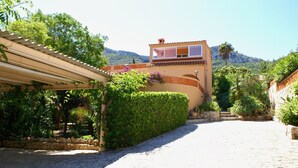 A villa with a stone pathway leading to a covered entrance, surrounded by lush greenery and a mountain backdrop. - Rustic villa with pool Marquesa GR (Denia)