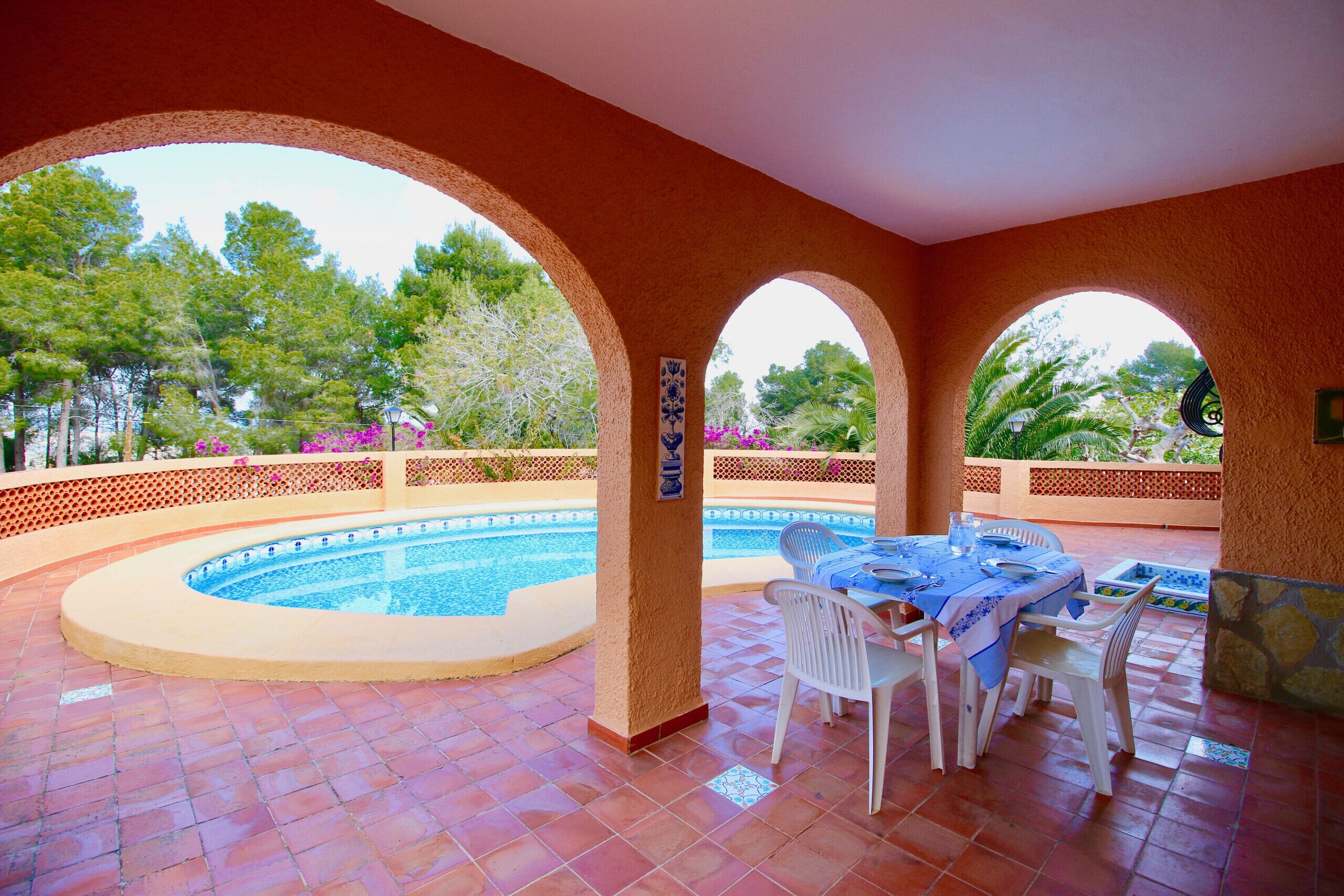 A covered outdoor area with a pool, dining table, and chairs.