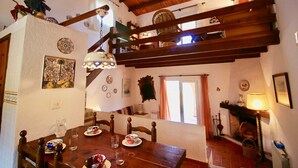A dining area with a wooden table, chairs, and a chandelier. There is a fireplace with a lamp, and a window with curtains. - Rustic villa with pool Marquesa GR (Denia)