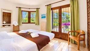 A hotel room with two beds, a wooden chair, a window with a view of greenery, and a door with a metal gate. - Villa Bellavista WA with Private Pool and Garden in Dénia (Denia)