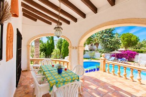 An outdoor patio with a pool, white chairs, and a table with a checkered tablecloth. - Villa Bellavista WA with Private Pool and Garden in Dénia (Denia)