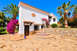 A white building with a tiled roof, a stone wall, and a paved courtyard with steps leading to the entrance. - Villa Bellavista WA with Private Pool and Garden in Dénia (Denia)