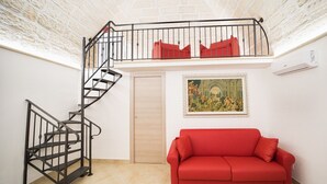 A room with a red sofa, a spiral staircase, a wooden door, and a framed painting on the wall.