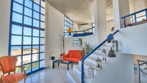 Un vaste espace de vie doté de grandes fenêtres, d’un canapé rouge, d’une chaise en bois et d’un escalier agrémenté de lanternes décoratives.