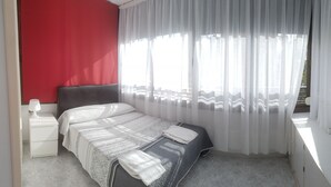 A bedroom with a bed, a nightstand, a red wall, and a window with sheer curtains. - GEMELOS 12(2 BEDROOMS) (Benidorm)